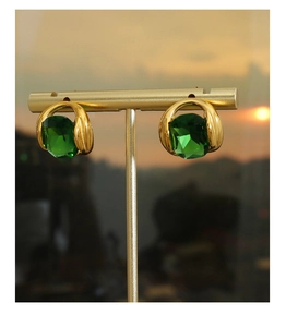 Détail de boucles d'oreilles en cristal émeraude sur un présentoir doré au coucher du soleil