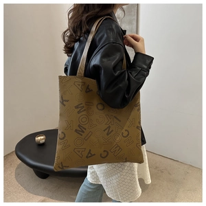 Brown leather tote bag with letter print shown on a model in a minimalist room