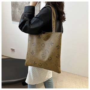 Detail of large brown tote bag showing textured faux leather and black letter patterns