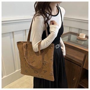 Detail of a large brown leather tote bag with letter prints in a cozy indoor setting