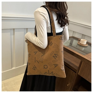 Detail of a brown leather tote bag with letter prints and long shoulder straps