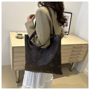 Close-up of a large dark brown tote bag with all-over letter print and slim shoulder straps