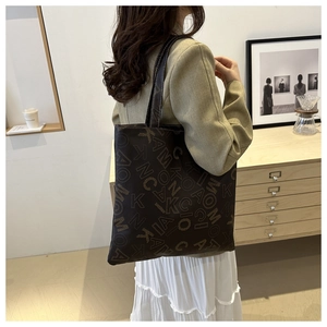 Detail of dark brown canvas tote bag with letter prints styled on woman shoulder