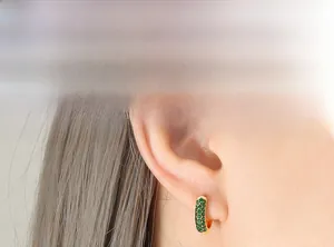 Close-up of gold hoop earrings with green zircon stones worn by a female model