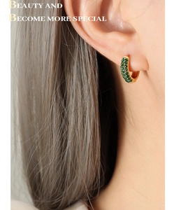 Detail of gold hoop earring with pavé-set green zircons worn on model's ear