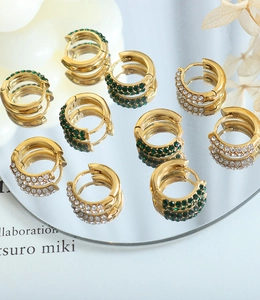 Close-up of gold-plated hoop earrings with emerald green and clear zircon stones