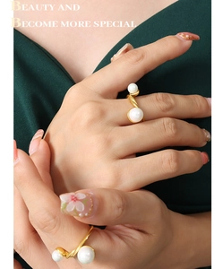 Gros plan d'une bague torsadée dorée avec deux perles blanches sur une main