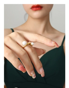 Détail d'une bague torsadée en or avec deux perles sur le doigt d'une femme