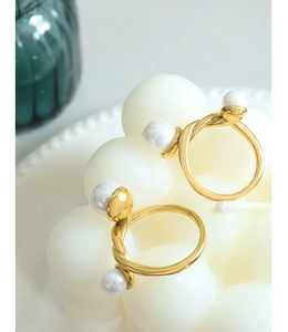 Détail de la bague en métal torsadé doré avec deux perles blanches sur une bougie