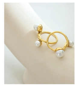 Détail d'une bague torsadée dorée ornée de perles blanches sur un support minimaliste