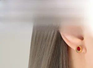 Gros plan d'un modèle portant une boucle d'oreille ovale en zircon rouge et cadre doré