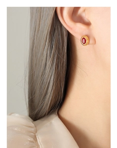 Gros plan d'une boucle d'oreille ovale dorée avec pierre rouge sur un modèle