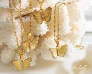 Détail du collier papillon doré avec zircons sur un présentoir en corail blanc