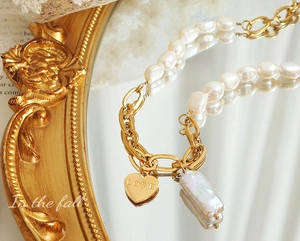 Detail von goldenem Herzanhänger mit LOVE-Gravur und Barockperle auf einer Vintage-Kette