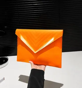Detail of orange envelope clutch featuring V-shaped stitching and gold metal edge