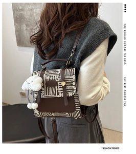 Detail of British style backpack featuring woven texture, leather flap, and plush cloud charm