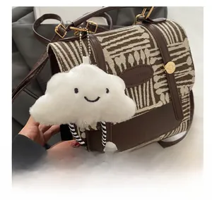 Close-up of white plush cloud charm with smiley embroidery on a vintage checkered bag