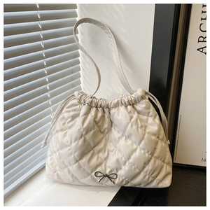 Detail of cream quilted leather tote bag with drawstring closure and metal bow accent