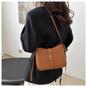Detail of a brown leather shoulder bag with a gold metal buckle and fine texture