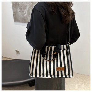 Detail view of large striped canvas tote bag with brown leather label and fashion logo