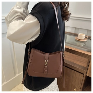 Detail of a brown leather crossbody bag with a gold infinity buckle on a model