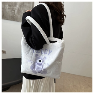 Close-up of white quilted tote bag featuring a cute purple teddy bear print and sturdy handles