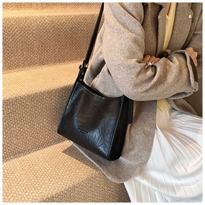 Fashionable black leather tote bag with embossed text worn by a model in a suit
