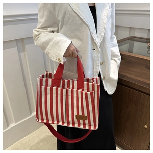 Detail of striped canvas tote bag with front pockets and red fabric handles