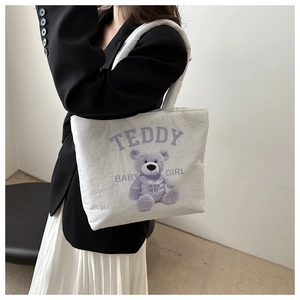 Close-up of quilted white canvas tote bag with purple teddy bear and artistic text