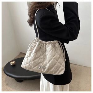 Detail of off-white quilted tote bag with drawstring closure and silver bow ornament