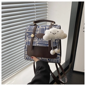 Detail of plaid canvas mini backpack with brown leather flap and cloud plush charm