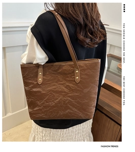 Detail of dark brown tote bag with crumpled texture and gold rivet reinforcements