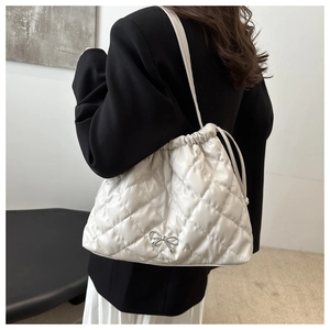 Close-up of white quilted tote bag featuring a silver bow detail and drawstring closure