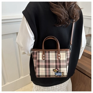 Detail der karierten Handtasche mit Dackel-Stickerei und braunen Lederriemen im Fokus