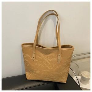 Detail of light brown tote bag featuring wrinkled texture and golden rivet shoulder straps