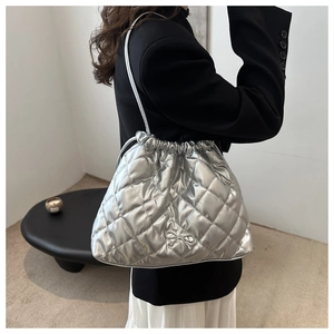 Detail of silver quilted bucket bag with bow accents and drawstring closure on model
