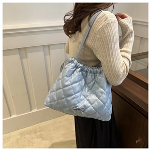 Close-up of quilted light blue bucket bag with metal bow pendant and drawstring detail