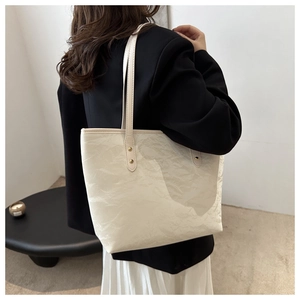 Detail view of the cream tote bag showing its unique pleated texture and gold rivets