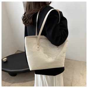 Detail of a creamy white tote bag with a crinkled texture shown on a shoulder