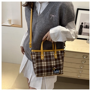 Detail einer Vintage-Handtasche mit braunem Karomuster, gelbem Ledergriff und Stickerei