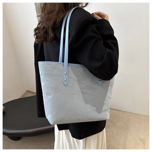 Detail of light blue tote bag featuring crinkled texture fabric and gold-rivet straps