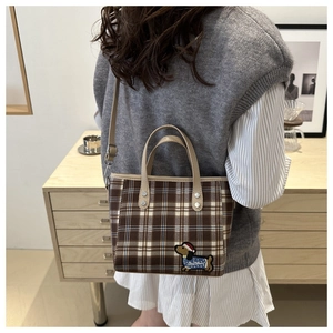 Detail einer Retro-Karohandtasche in Braun mit süßer Hundestickerei und Ledergriff