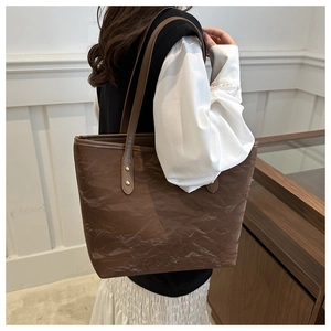 Detail view of brown large tote bag with pleated leather texture and gold rivet hardware