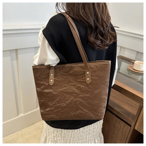 Detailed texture of brown pleated tote bag with slim shoulder straps on a model