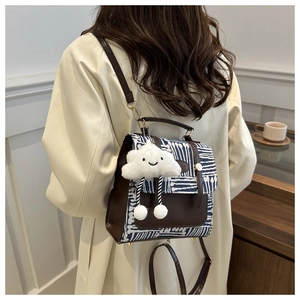 Detail of a brown leather backpack with blue abstract pattern and white plush pendant