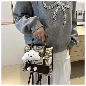 Close-up of British style geometric satchel with cute white cloud plush pendant accessory