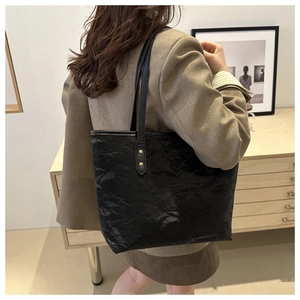 Detail of black tote bag with wrinkled leather texture and golden rivet accents