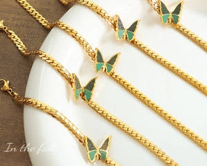 Detail von goldenen Panzerketten-Armbändern mit grün emaillierten Schmetterlingsanhängern