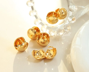 Detailed view of polished gold dome huggie earrings with a functional hinge mechanism