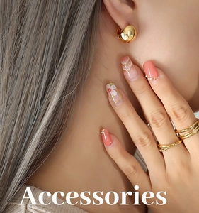 Detailed view of polished gold C-shape ball earrings and layered rings on a model